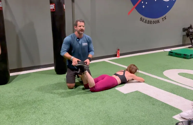 Trainer assisting woman in leg stretch exercise at gym.